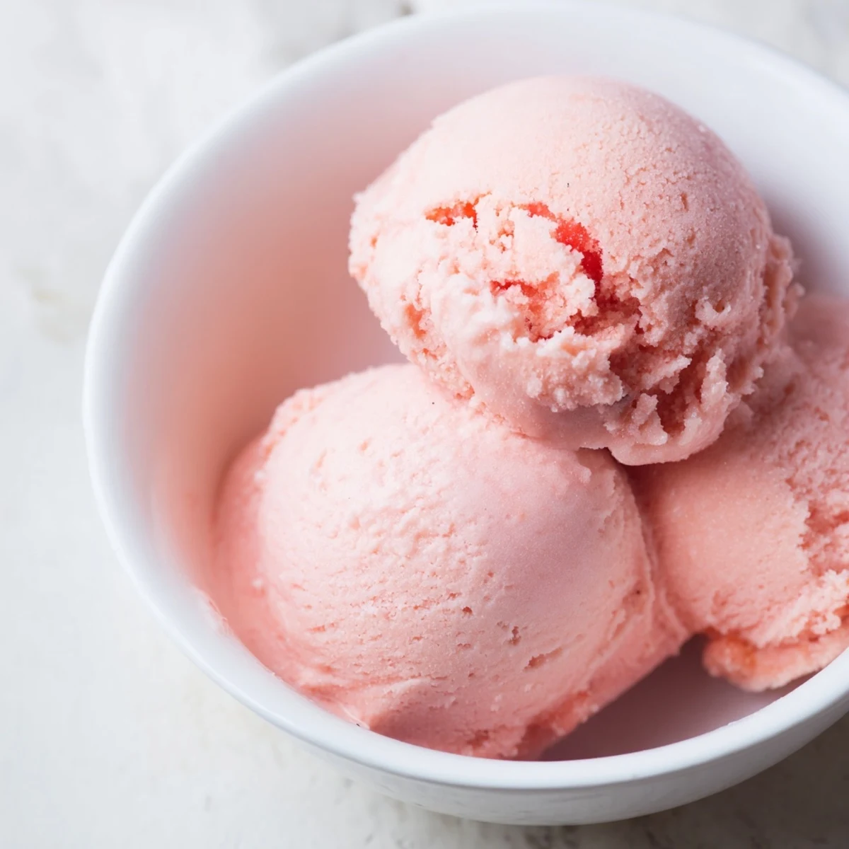 Vibrant pink watermelon ice cream sitting in a vintage metal ice cream scoop