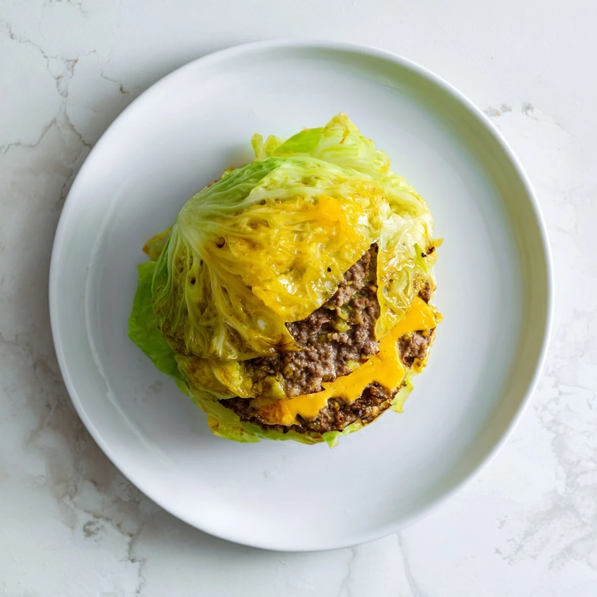 Golden brown oven baked cabbage burger wrapped in tender green cabbage leaves on a white plate