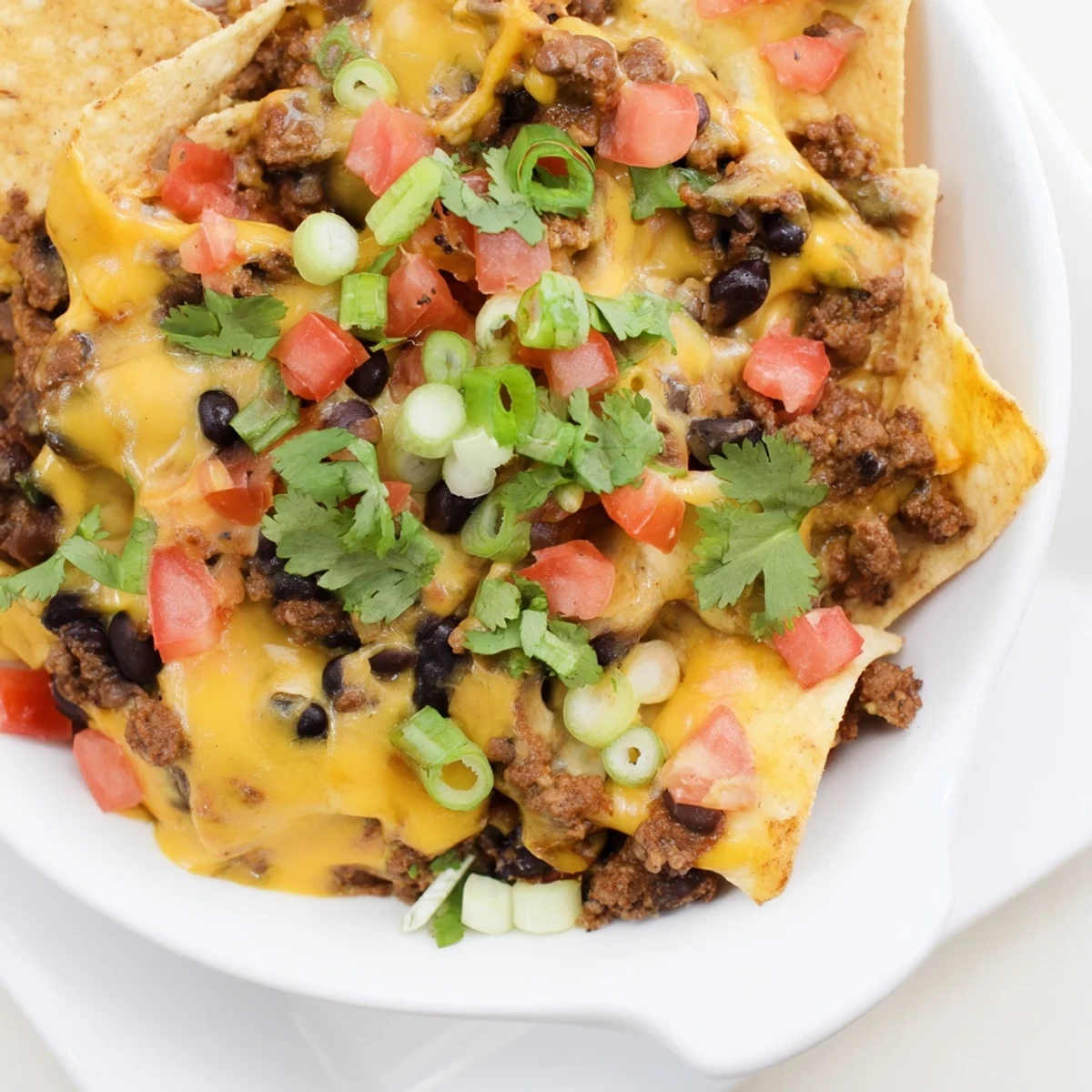Tex-Mex style Super Nachos Dip bubbling in a serving bowl with layers of spiced meat, cheese, and vegetables