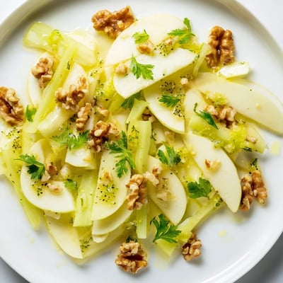 Walnut-tossed apple and celery salad served in a white bowl, featuring fresh parsley and a glossy light lemon dressing.
