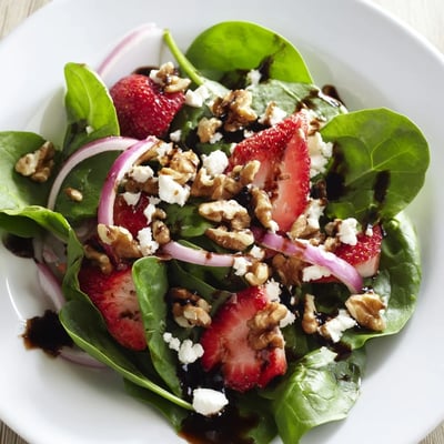 A close-up of a colorful Strawberry Spinach Salad with Walnuts featuring juicy berries, toasted nuts, and a tangy vinaigrette, ready to serve at a summer picnic.
