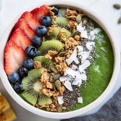 Vibrant green smoothie bowl filled with spinach and kale, finished with kiwi, blueberries, and pumpkin seeds for texture.  